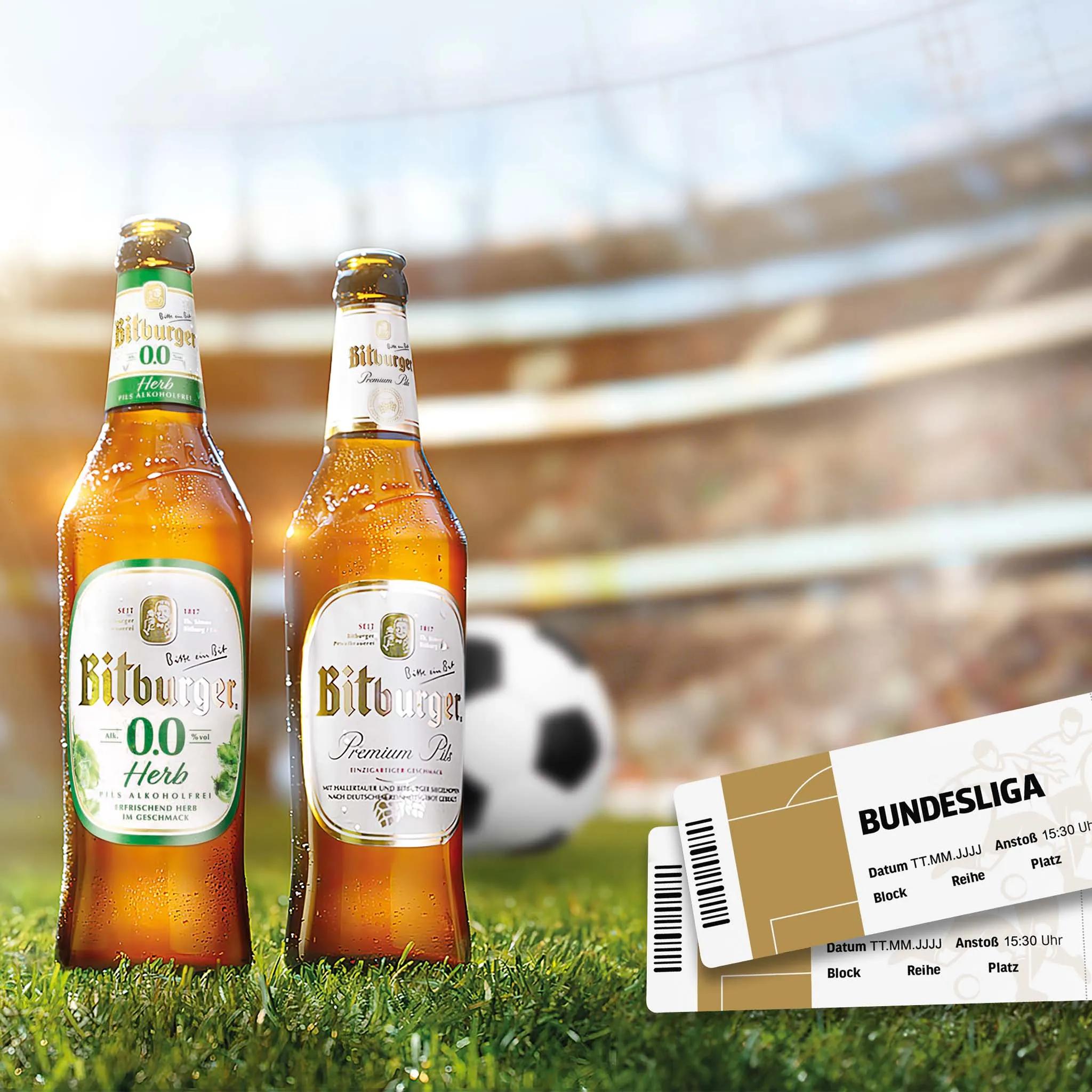 Zwei Bitburger-Bierflaschen auf dem Rasen vor einem Fußballstadion mit Fußball und Bundesliga-Tickets.