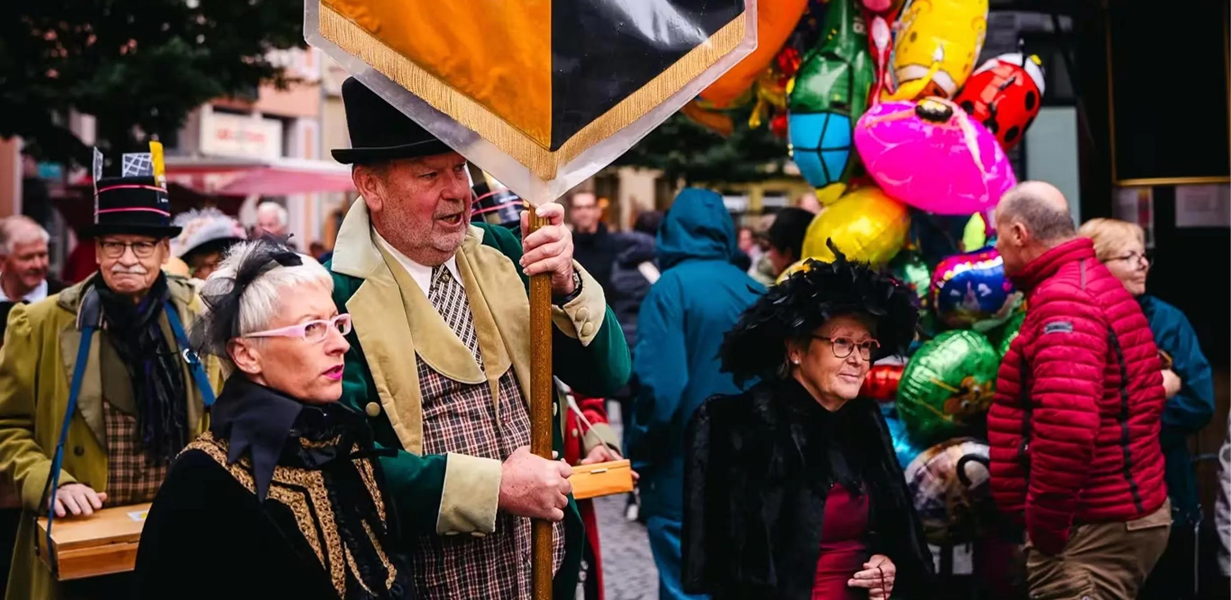 Gruppe an verkleideten Personen läuft mit einer Flagge durch eine Straße.
