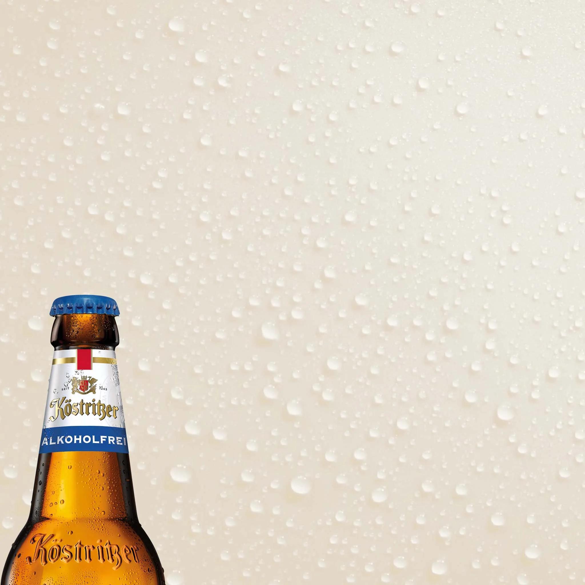 Flaschenhals eines alkoholfreien Bieres in der unteren linken Ecke vor einem neutralen Hintergrund mit Wassertropfen.