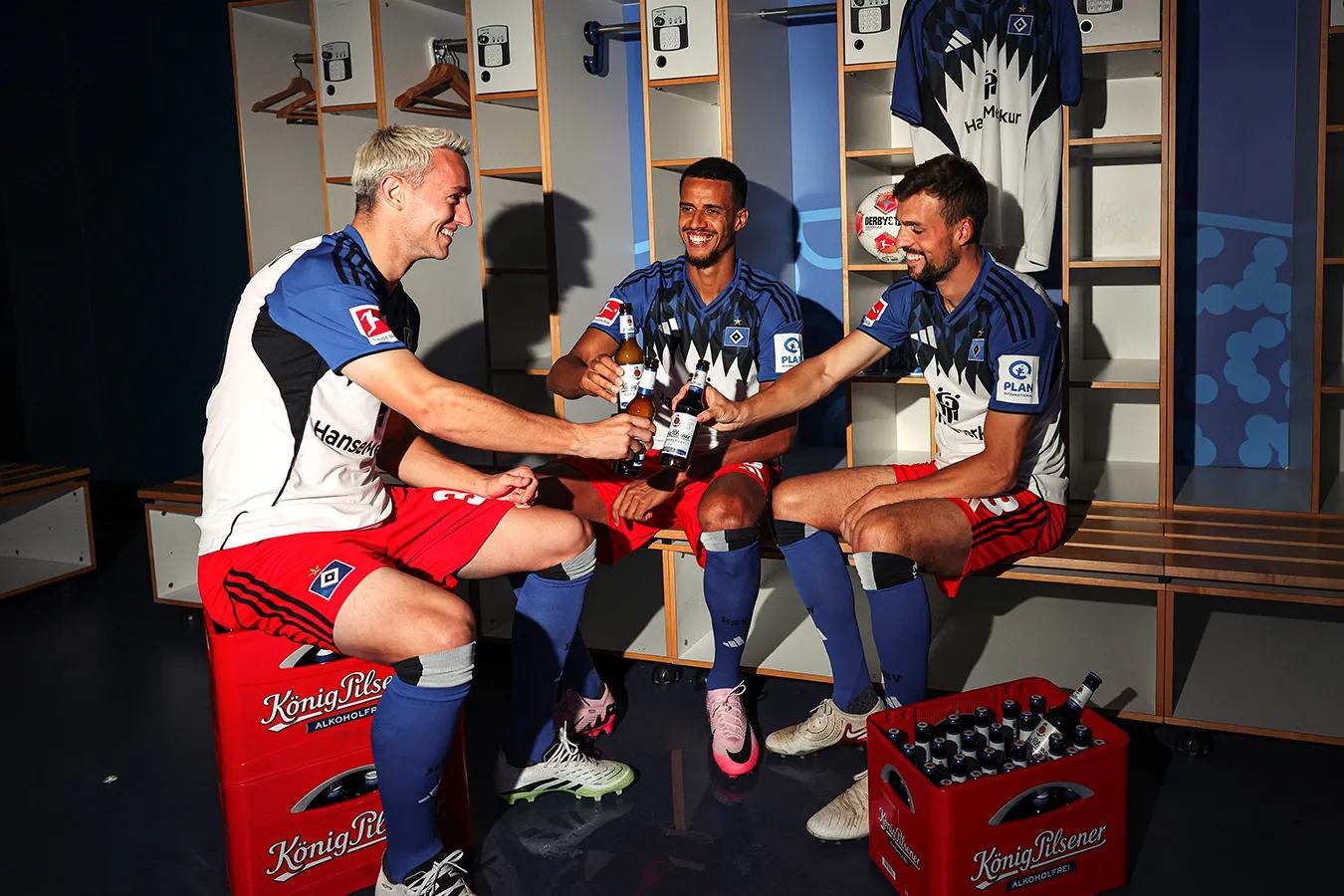 Drei Fußballspieler in der Umkleidekabine trinken gemeinsam Bier nach dem Spiel.