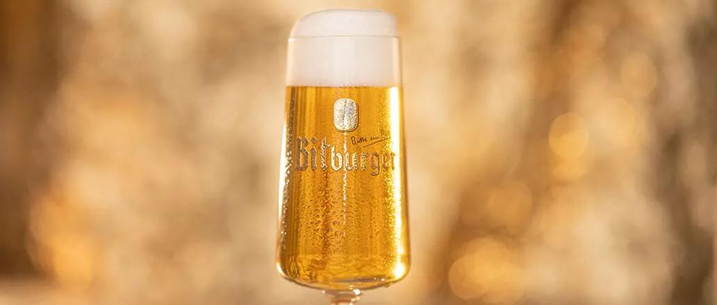 Bitburger Pils Glas gefüllt mit Bier vor goldenem Hintergrund