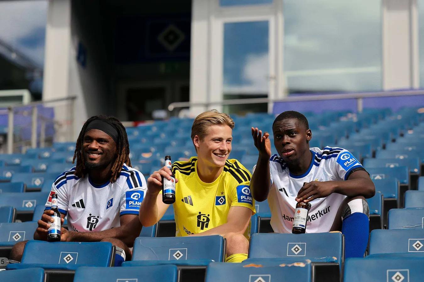 Teamfoto HSV: 3 Fußballer sitzen alleine auf der Tribühne.