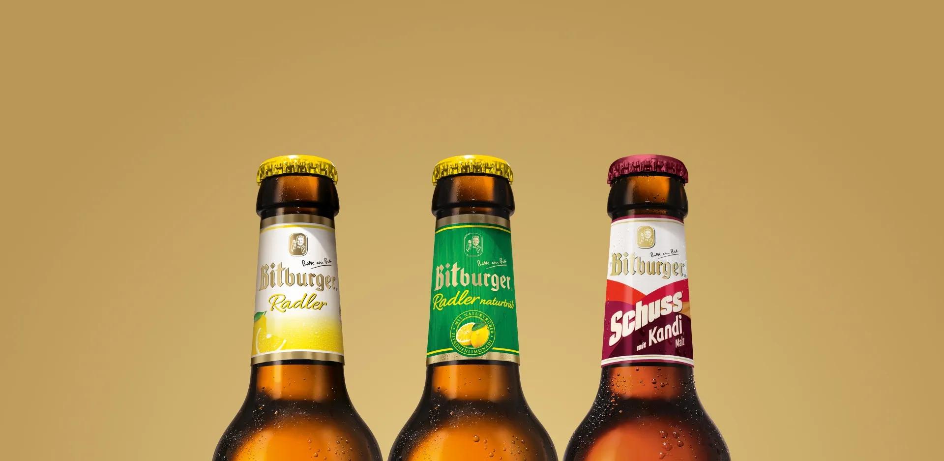 Das obere Drittel von drei Flaschen der Bitburger Biermixe auf goldenem Hintergrund.