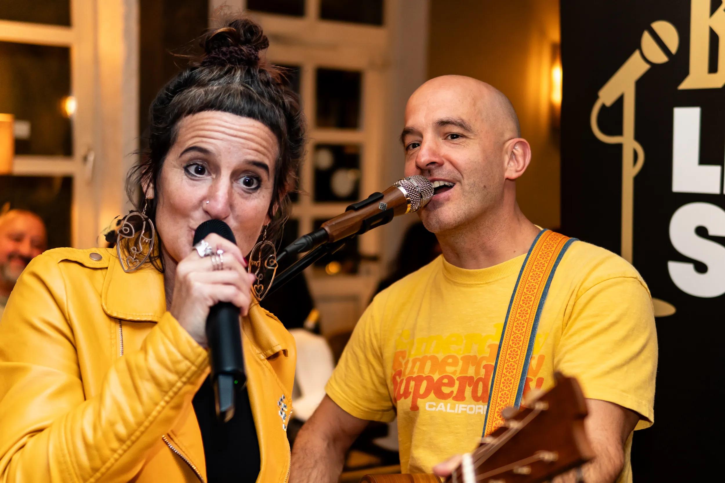 Zwei Personen in gelbem Outfit singen bei einer Veranstaltung.