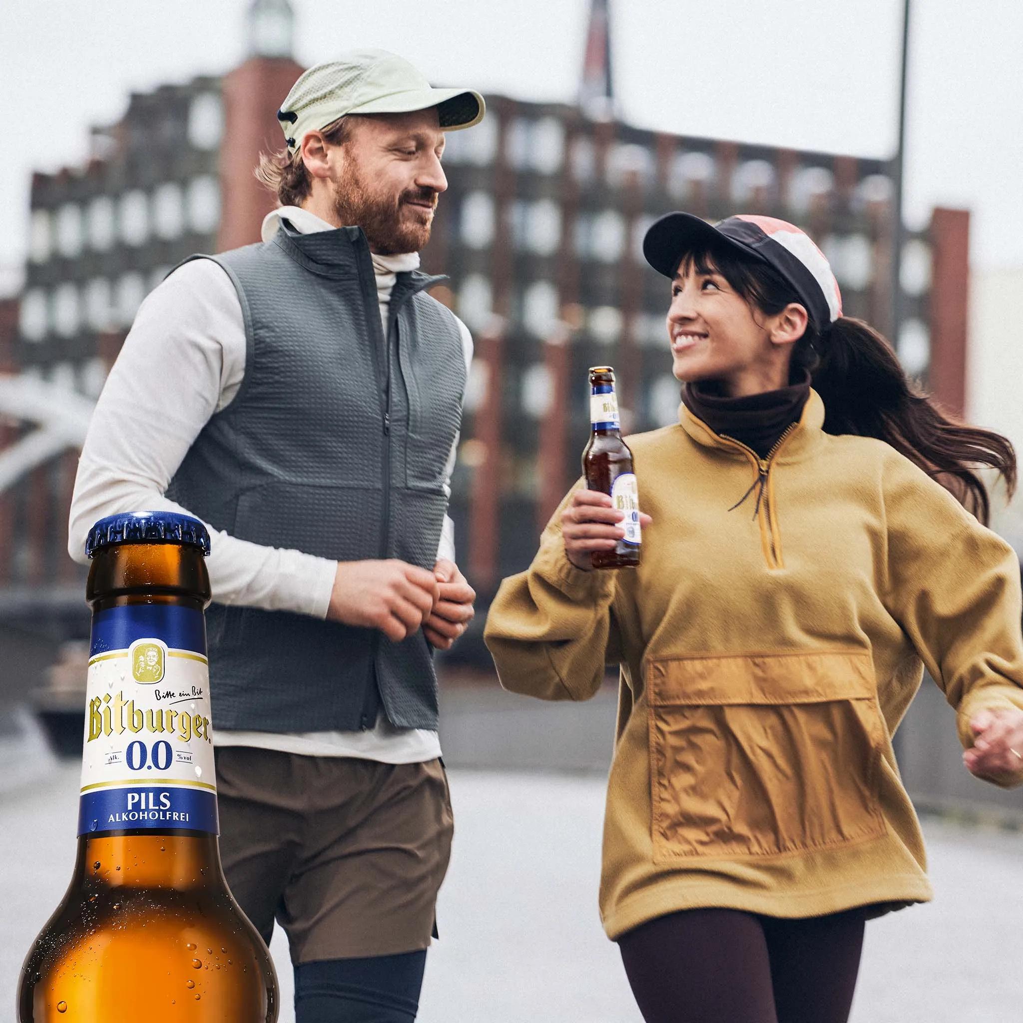 Zwei Läufer:innen laufen nebeinenander, eine Person hält eine Flasche Bitburger Alkoholfrei.