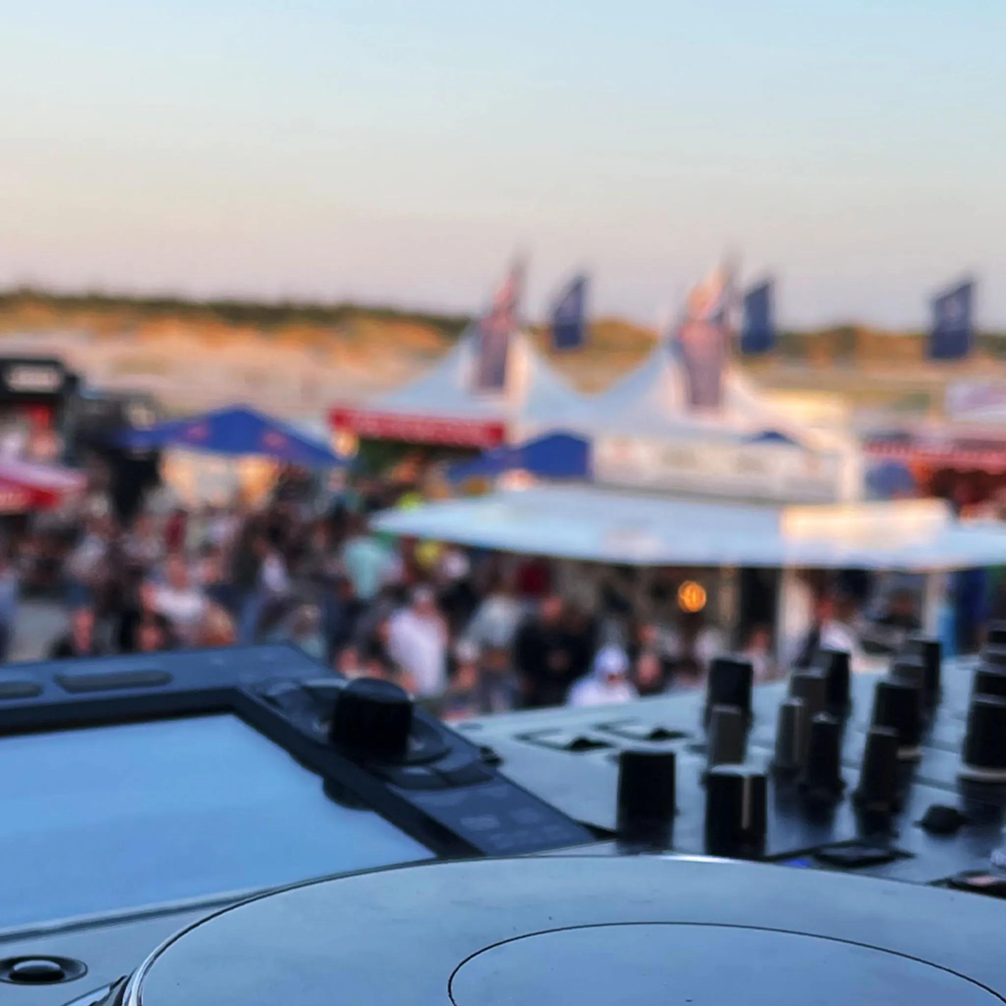 Kitesurf Masters, Nahaufnahme eines DJ Pults, im Hintergrund Abenddämmerung am Strand mit Menschen auf dem Festivalgelände