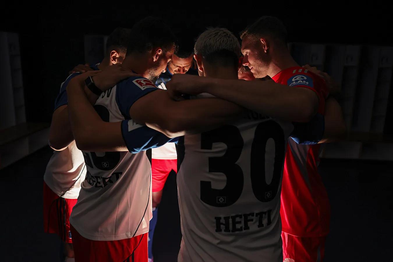 Fußballspieler stehen sich umarmend im beleuchteten Kreis in einem dunklen Raum.