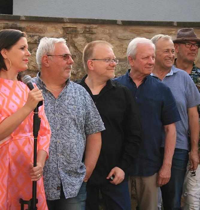 5 Personen stehen hintereinandergereiht vor einem Mikrofon.