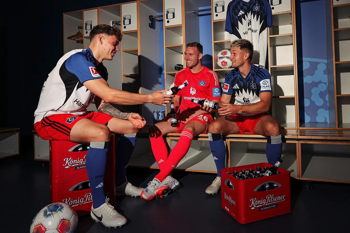 Drei Fußballspieler in der Umkleidekabine trinken gemeinsam Bier nach dem Spiel.
