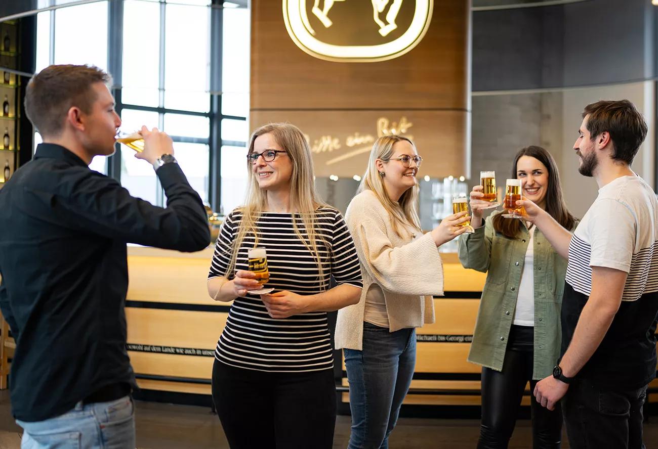 Bitburger Erlebniswelt, eine Gruppe steht an der Theke und prosten sich mit einem Bier zu.