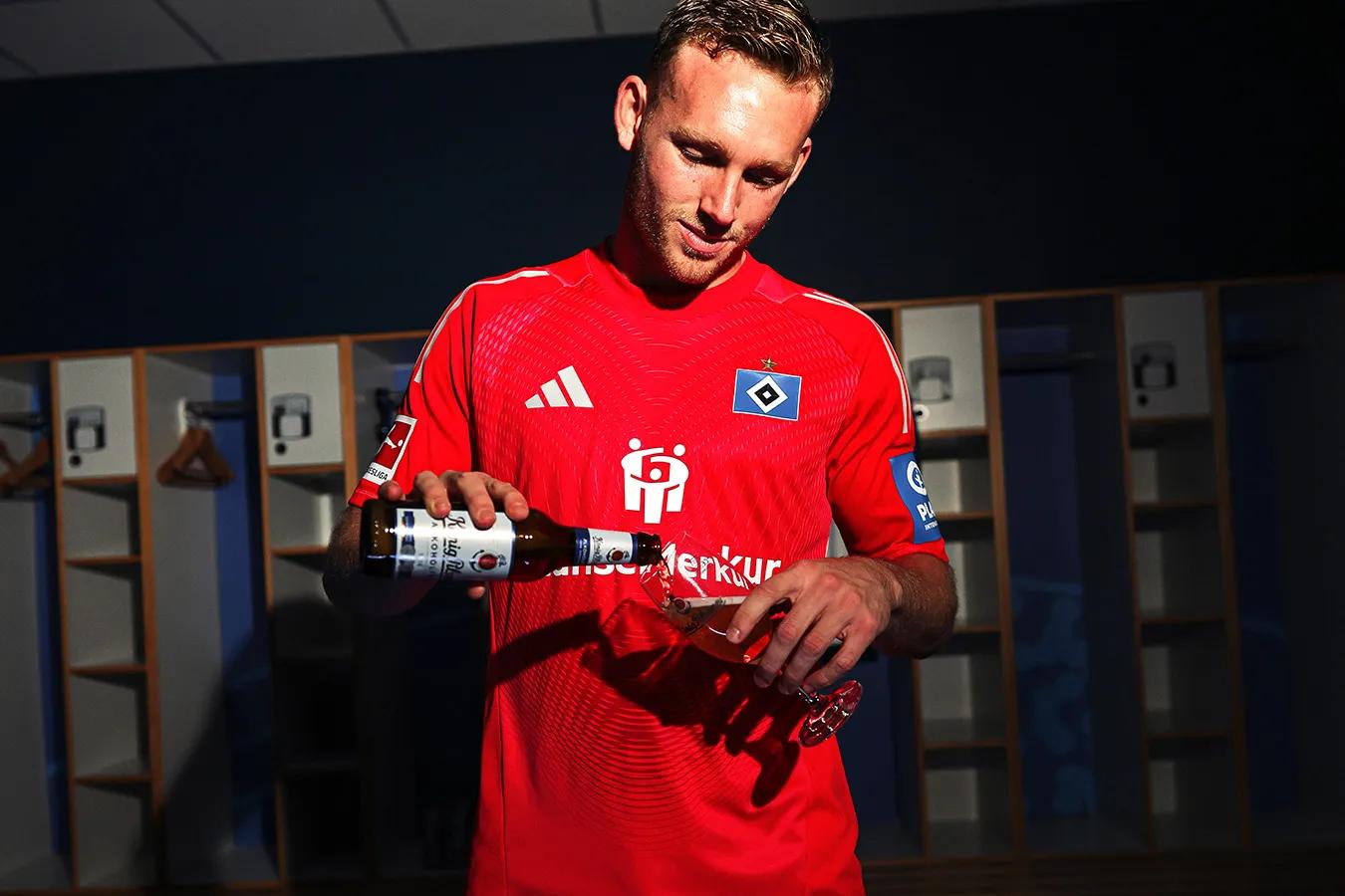 Ein Fußballspieler schenkt sich ein Glas König Pilsener aus einer Flasche ein.