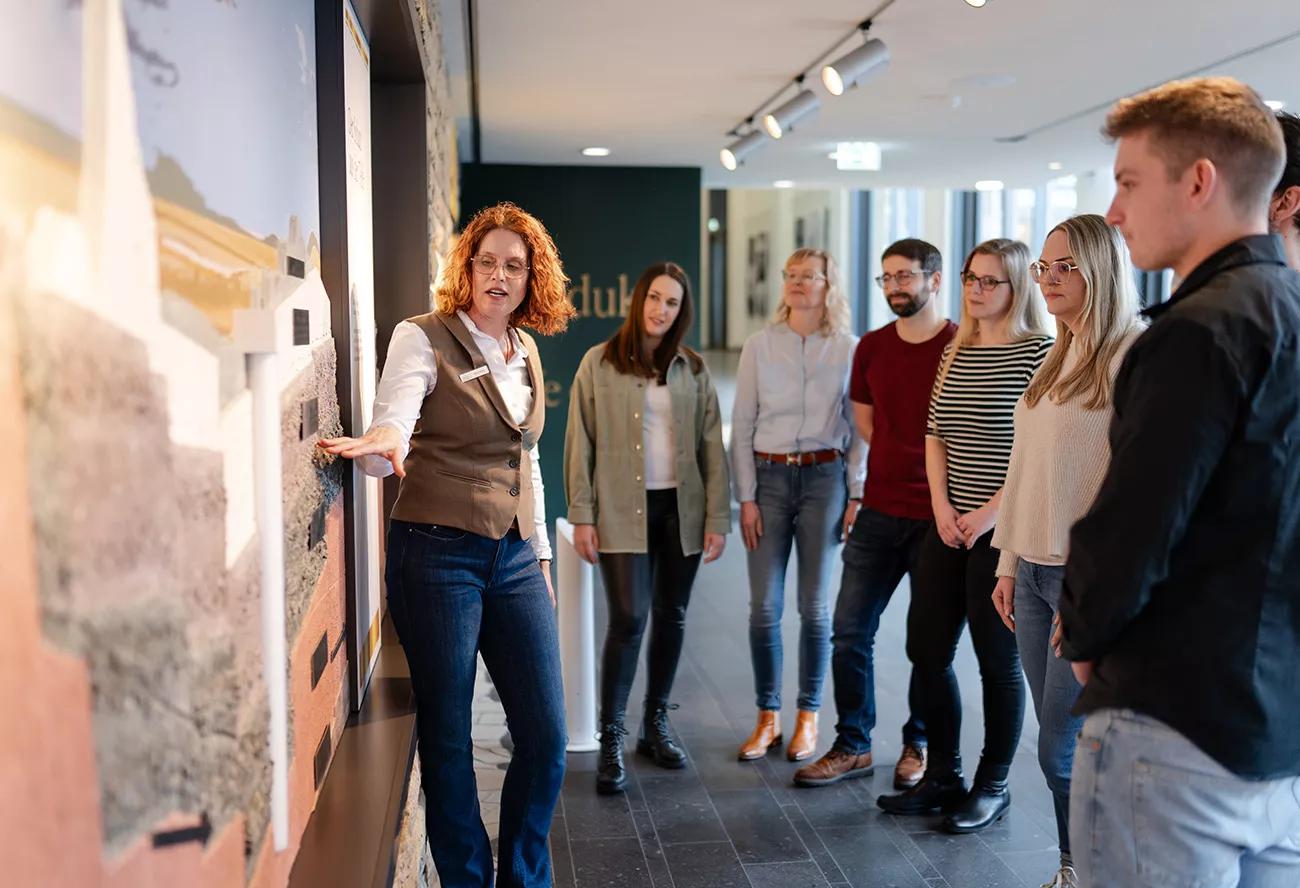 Bitburger Erlebniswelt, eine Gruppe steht vor einer Karte, auf die eine Frau erklärend zeigt