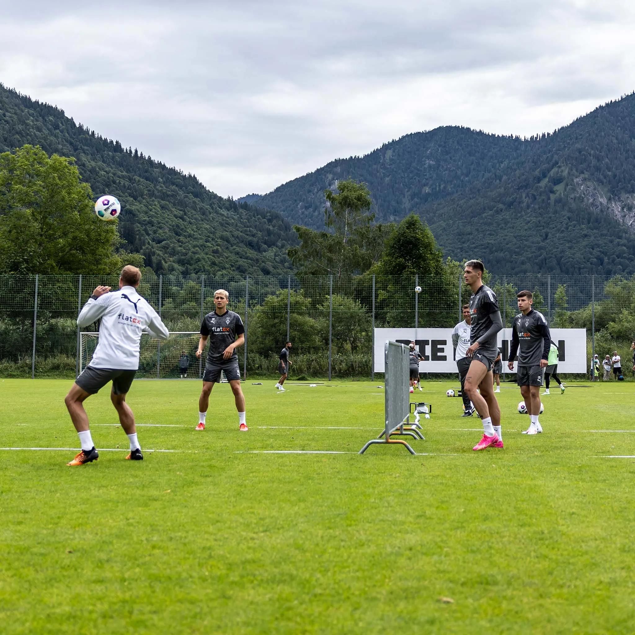 Foto vom Trainingslager Borussia Mönchengladbach. Spieler spielen Fußball auf dem Fußballfeld. Im Hintergrund ist eine bergige Landschaft zu sehen.