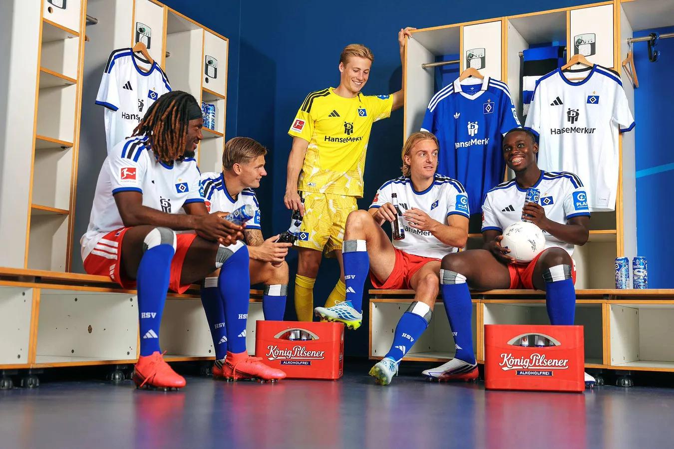 Teamfoto HSV : 5 Fußballer sind in der Umkleidekabine mit 2 Kästen König Pilsener und erzählen.