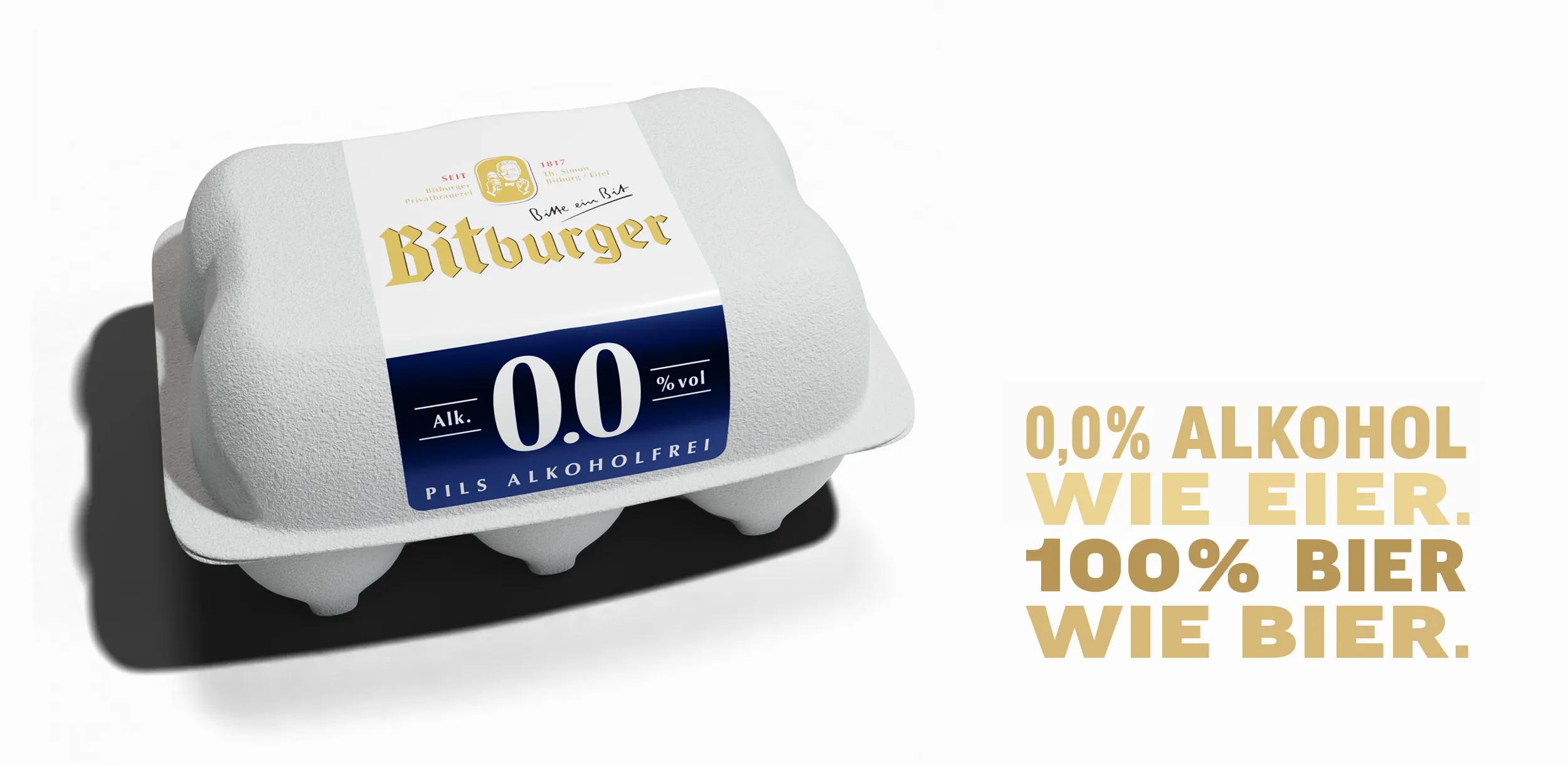 Rechts unten steht in goldener Schrift: „0,0% ALKOHOL WIE EIER. 100% BIER WIE BIER.“ Links oben steht eine Verpackung, die optisch einem Eierkarton ähnelt, aber mit der Bitburger 0.0%-Marke gestaltet ist. Die Verpackung kombiniert Weiß, Gold und Dunkelblau und trägt die Aufschrift „Bitburger Pils Alkoholfrei 0.0% vol“. Der Hintergrund ist weiß.