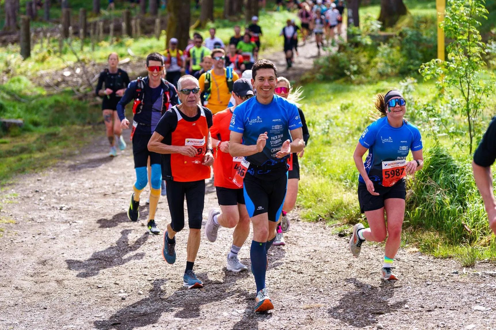 Eine Gruppe von Läufern mit ist auf einem Waldweg unterwegs.