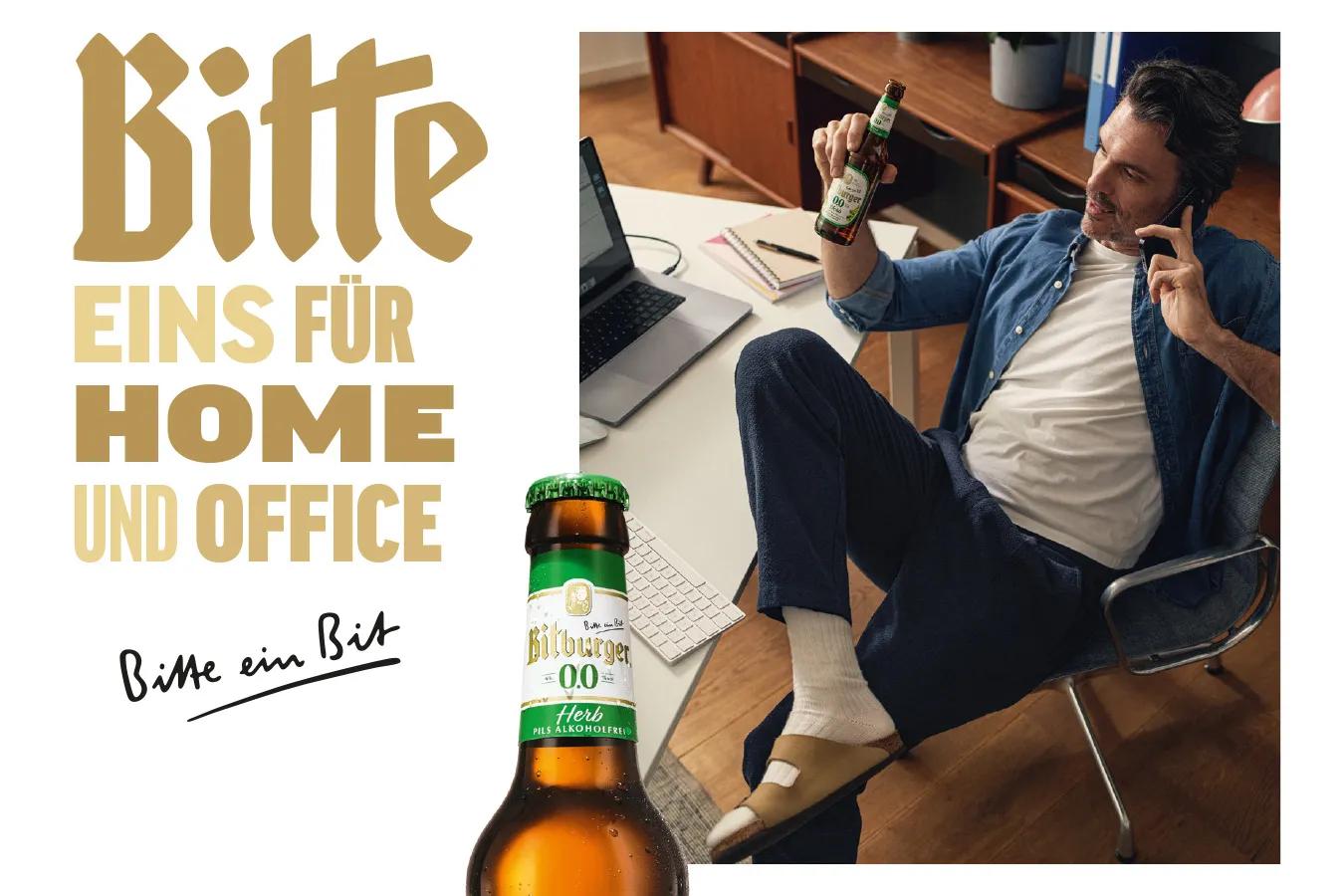 Bitburger Kampagnenmotiv - "Bitte eins fürs Home und Office" - Mann sitzt lässig am Schreibtisch und hält eine Flasche alkoholfreies Bitburger in der Hand.