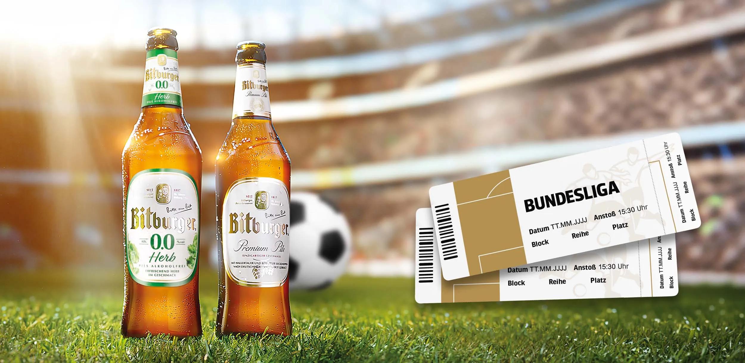 Zwei Bitburger-Bierflaschen auf dem Rasen vor einem Fußballstadion mit Fußball und Bundesliga-Tickets.