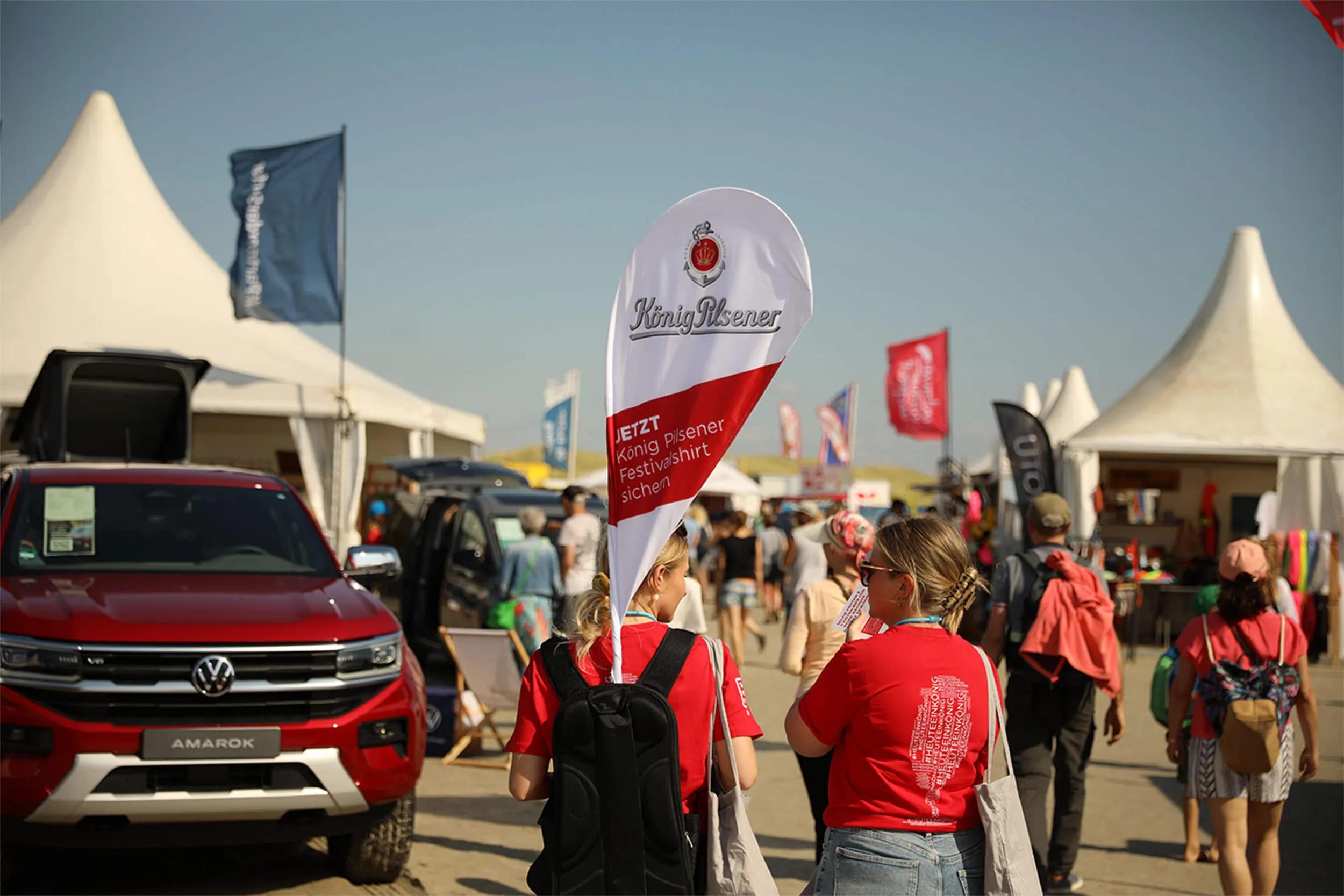Promoterinnen mit Flaggen auf belebtem Festivalgelände.