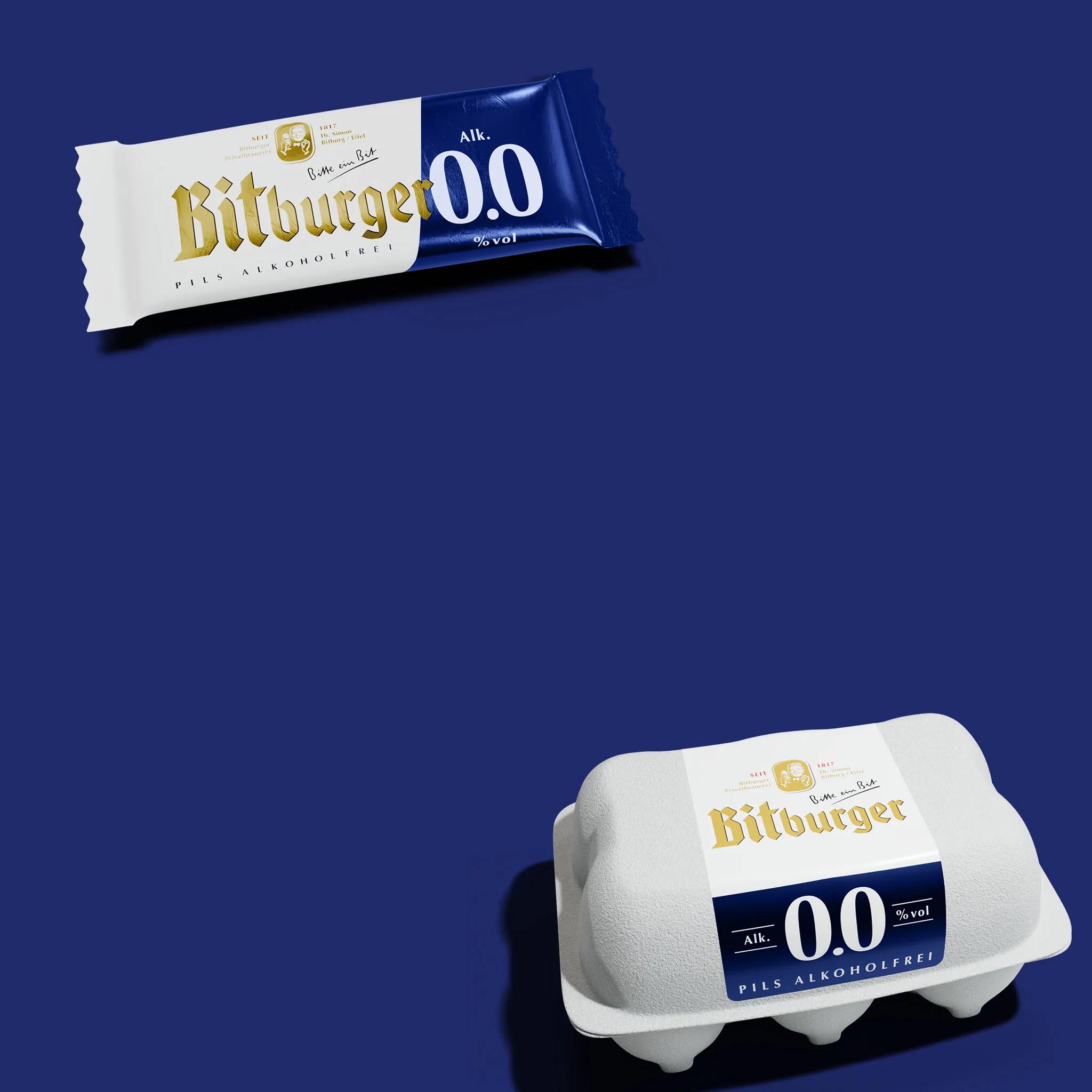 Oben links ist ein Riegel mit der Aufschrift "Bitburger 0.0 Pils Alkoholfrei" zu sehen. Unten rechts befindet sich eine Eierkarton Verpackung mit dem gleichen Schriftzug. Der Hintergrund ist tiefblau, hervorgehoben sind die weißen und goldenen Designelemente der Verpackungen.
